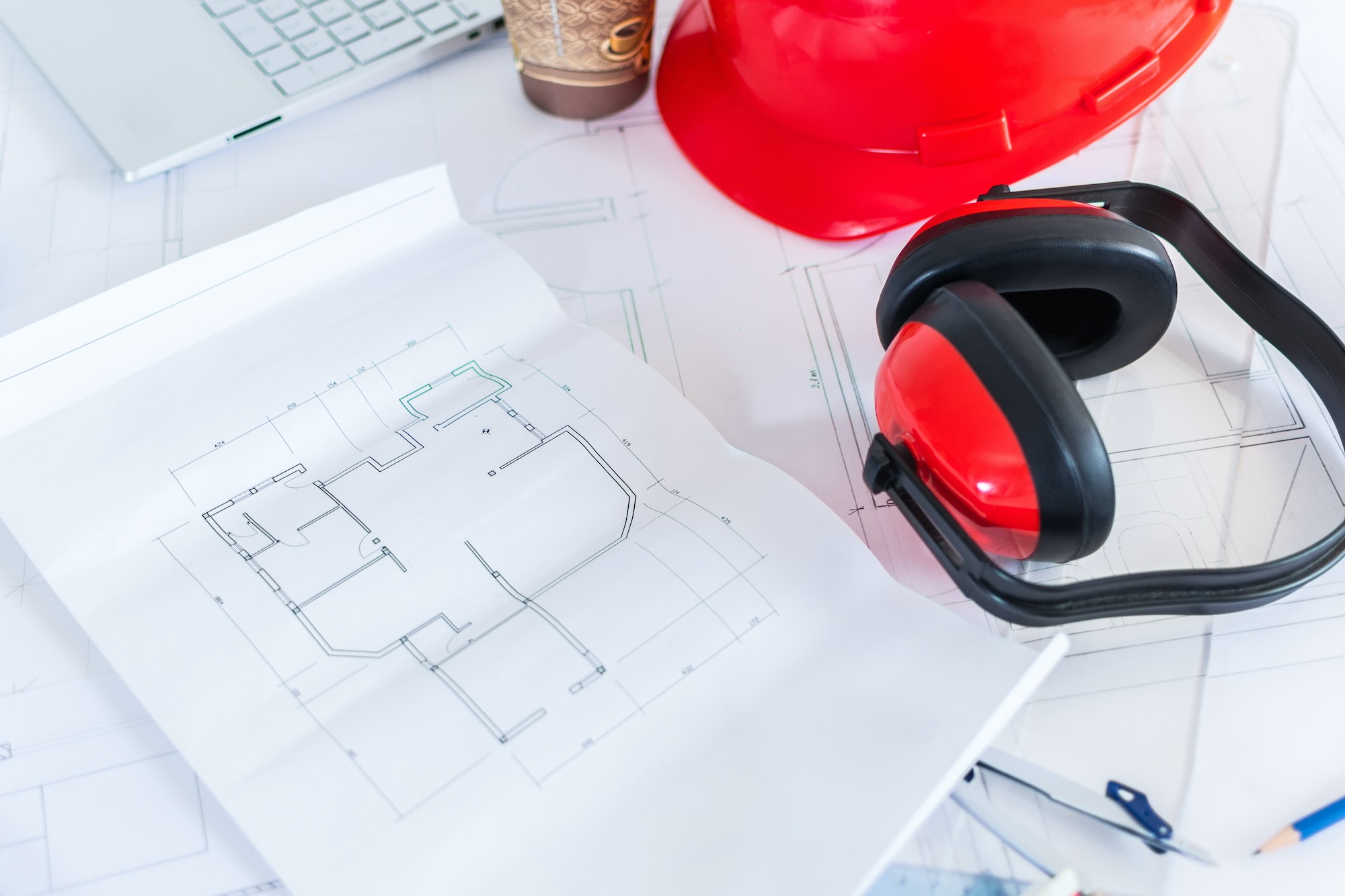 Closeup of construction blueprints with safety earmuff and helmet on the top